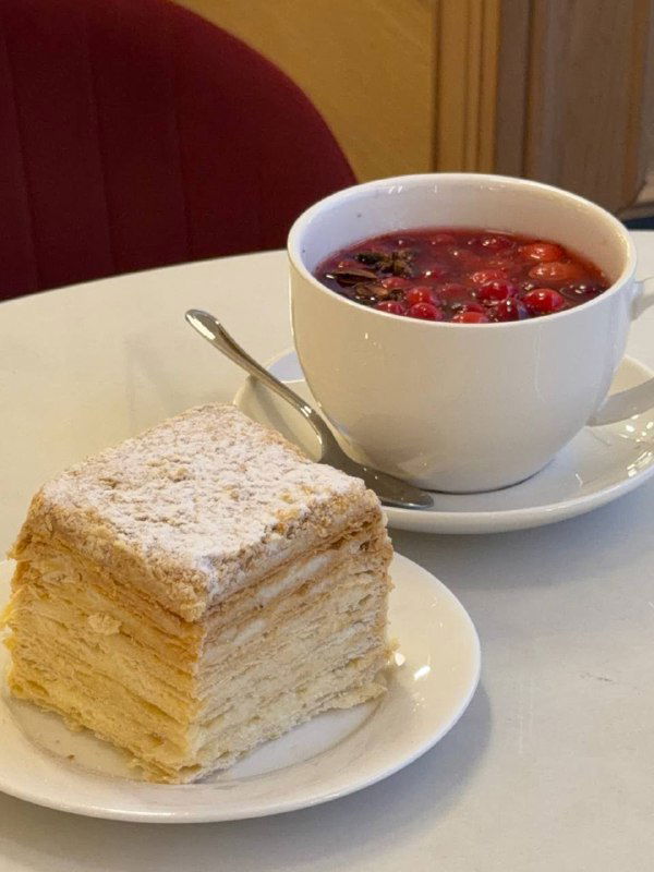 Крупный план кусочка Наполеона и чашки с ягодным горячим напитком на столе в сети Север‑Метрополь, видна текстура слоёного теста и пудра.