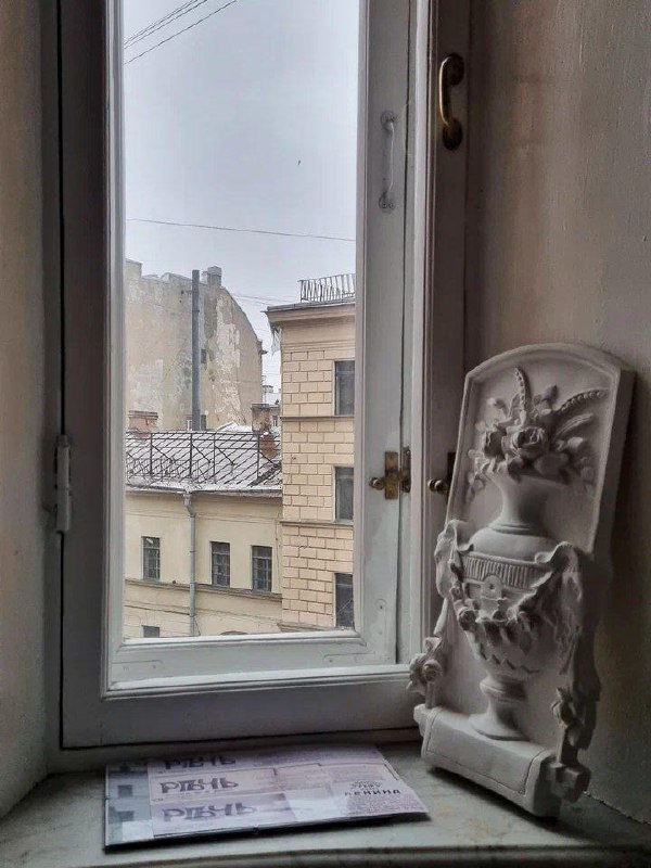 Вид из просторного окна Дома Бака на крыши петербургских зданий; на подоконнике — гипсовая декоративная скульптура и журналы.