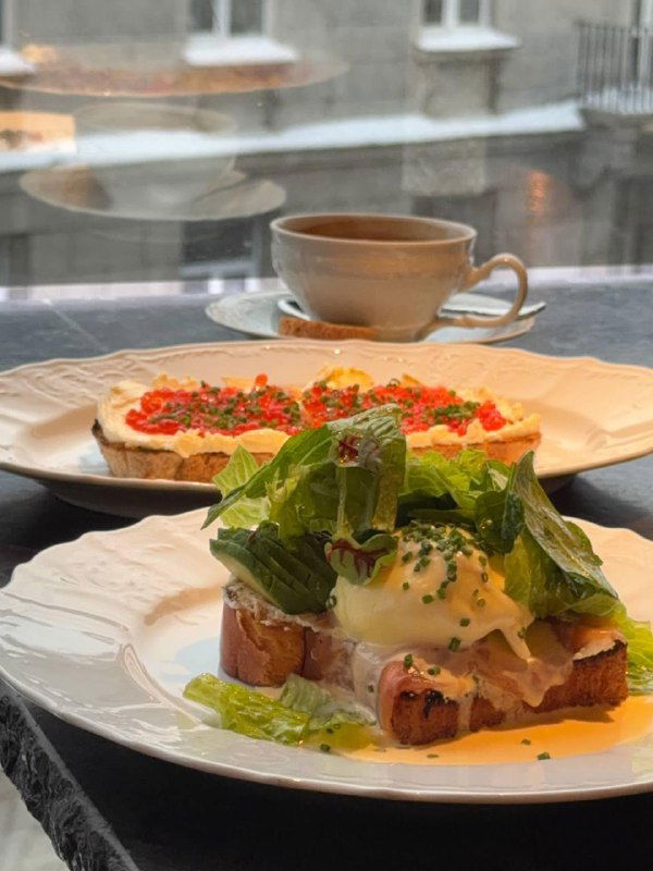Крупный план: бенедикт с форелью и бутерброд с красной икрой рядом с чашкой кофе у окна Tetto в Петербурге — подача и текстуры блюд видны чётко.