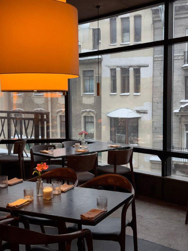 Зал Tetto у больших окон с видом на заснеженную улицу П.С., деревянные столы и тёплое освещение лампы создают атмосферу спокойного утреннего кафе.