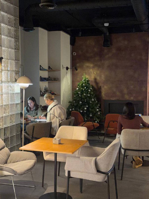 Зал Port Lounge с минималистичной мебелью, креслами и посетителями; на заднем плане небольшая украшенная ёлка и спокойная уютная атмосфера.