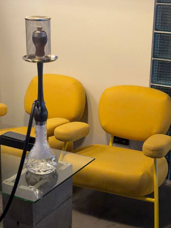Кальян на стеклянном столе рядом с ярко-желтыми креслами в отдельной зоне — оформление для комфортного отдыха с кальяном.