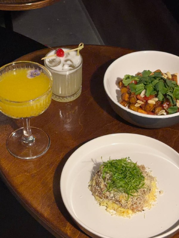 Стол с коктейлями и двумя блюдами: пармантье с уткой конфи и хрустящие баклажаны с арахисом, вид близко демонстрирует текстуру блюд.