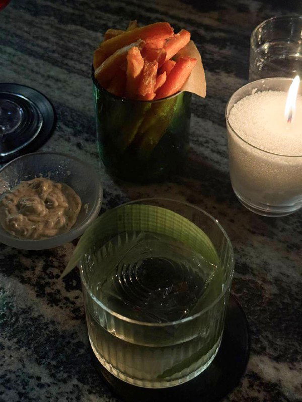 Порция батата фри в стакане рядом со свечой и стаканом воды на мраморной столешнице — деталь подачи и акценты освещения в Infuse.