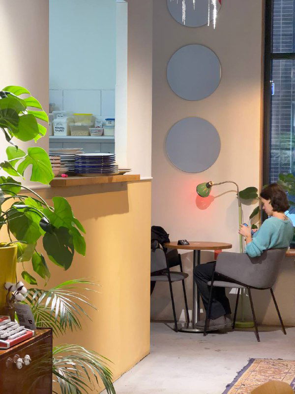 Уютный уголок кафе 8:am: большие зелёные растения, круглые декоративные элементы на стене, гости за столиками и мягкое дневное освещение в интерьере.