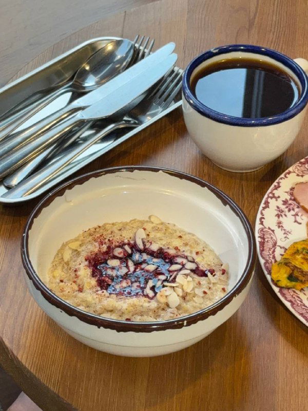 Миска овсянки на кокосовом молоке со смородиной, рядом чашка кофе и поднос с приборами — подробность завтрака в 8:am на Лесной.