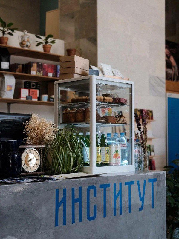 Барная стойка и витрина с выпечкой, бутылки и декор в индустриальном стиле; вид на часть кассы и прилавка в кафе.