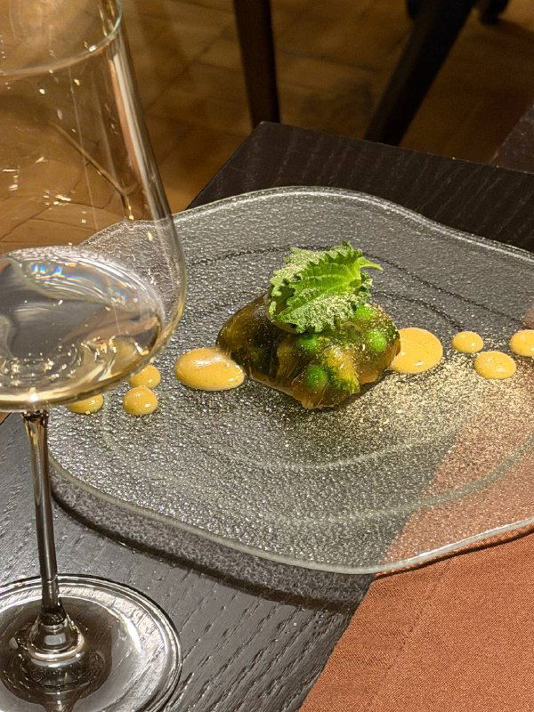 Аутентичная порция из серой тарелки с зелёным соусом и яркими элементами рядом с бокалом для вина — пример винного сопровождения к сету