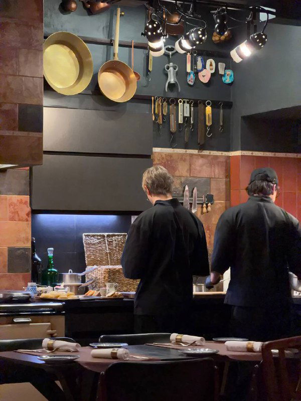 Открытая кухня ресторана ЕМ: повара в тёмной одежде готовят на фоне стен с висящей посудой и инструментами, видно рабочий процесс