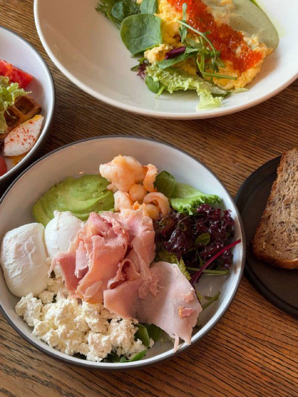 Тарелка-конструктор: креветки, окорок, микс салата, авокадо и рикотта — вид сверху, яркие ингредиенты и кусок северного хлеба рядом.