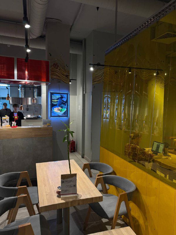 Ещё один ракурс интерьера Asiatiq: пустой стол, стулья и барная зона на заднем плане с прозрачной жёлтой перегородкой.