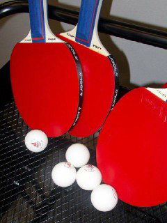 Крупный план трёх красных ракеток и нескольких белых мячей для настольного тенниса, подготовленных для игры.