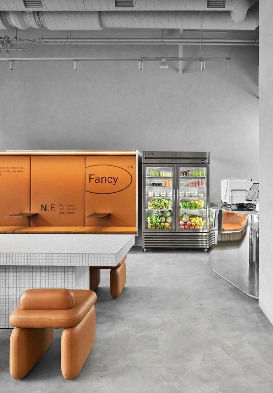 Интерьер кафе Nothing Fancy в спокойной цветовой гамме: минималистичный зал с оранжевыми пуфами, стойкой и холодильником с напитками, городской антураж.
