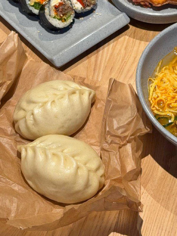 Пара традиционных пегоди в упаковке и краешек миски рамёна: паровые булочки рядом с супом, фото крупным планом на столе.