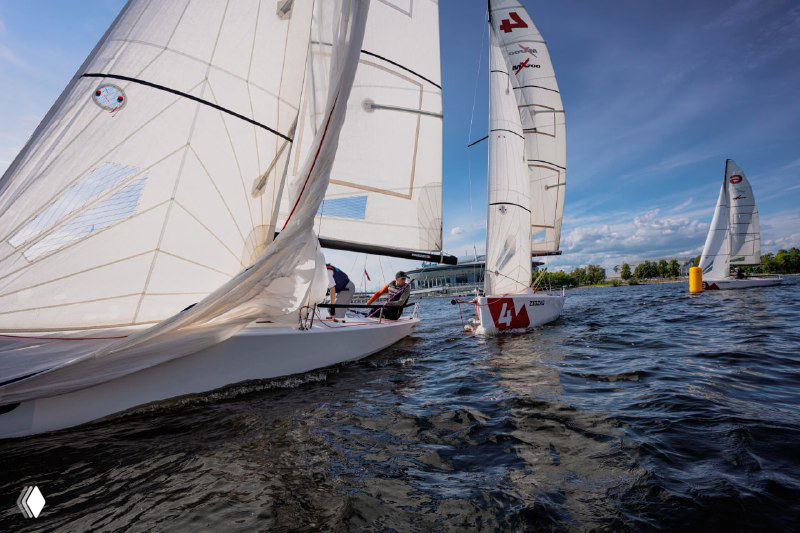 Несколько гоночных яхт с парусами во время соревнования; динамичная сцена командной работы на борту.