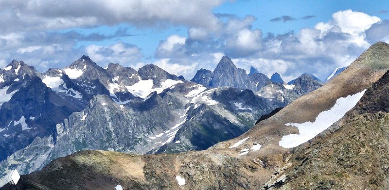 Горный хребет с участками снега и голыми скальными гребнями — панорама, иллюстрирующая альпийский рельеф вокруг Домбая летом.