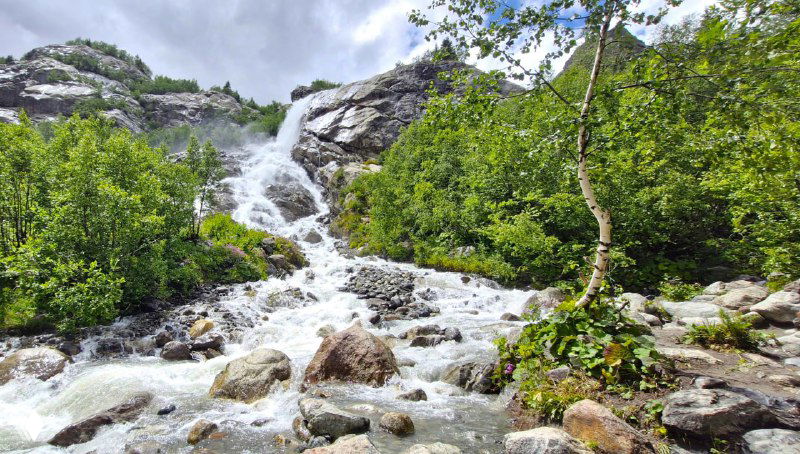 Бурный горный водопад между скалами и кустарниками — пример водных пейзажей, которые можно увидеть на однодневных маршрутах Домбая.