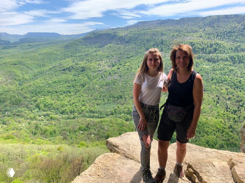 Дочь и мать стоят на гранитном выступе скалы, позируют на фоне густого леса и далёких горных хребтов, момент из семейного похода к Орлиной полке.