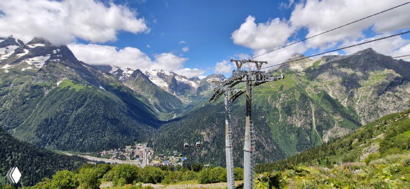 Опоры канатной дороги на фоне зелёных склонов и горных вершин Домбая, кабели тянутся через долину к следующей станции.
