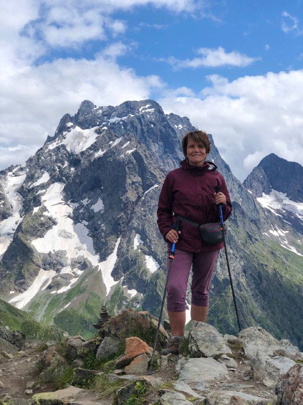 Туристка в треккинговой экипировке стоит на каменистом гребне, за ней массивная скалистая вершина Мусса-Ачитары.