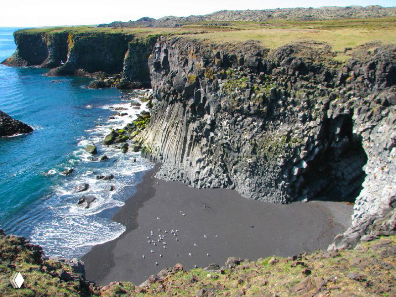 Обрывистые скалы и чёрный песчаный пляж у побережья Снэфетлснес — резкие скальные формы над морской гладью.