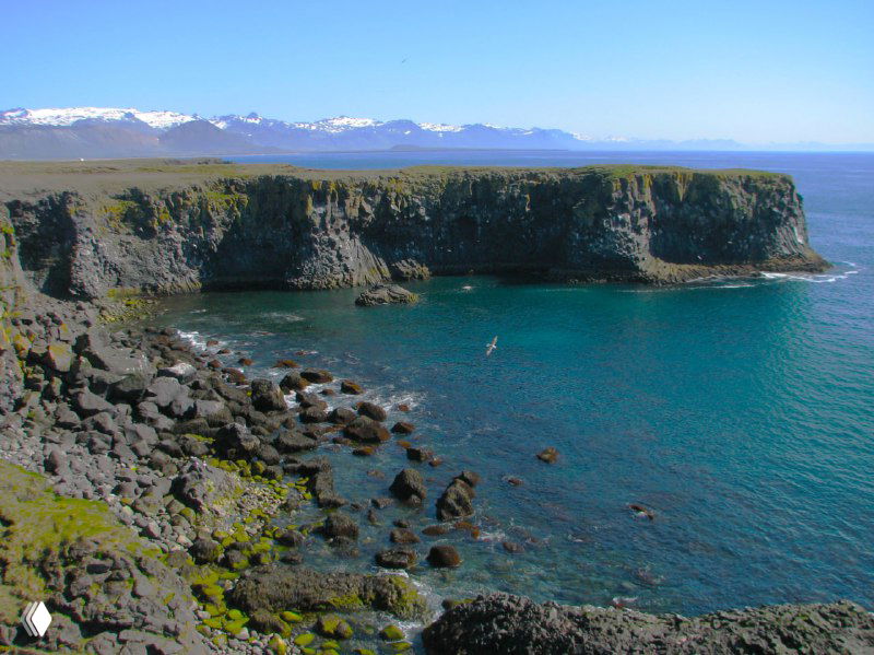 Залив с зелёными скалами и бирюзовой водой у побережья полуострова; вид на утёсистые берега рядом с тропой.