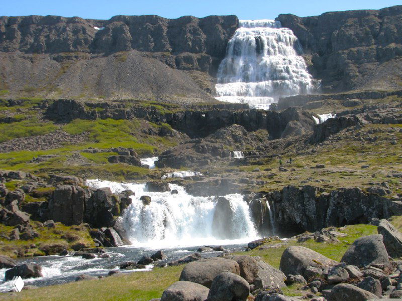 Широкий вид на водопад Диньянди: каскады воды стекают по склону, вокруг — скалистые уступы и зелёные участки.