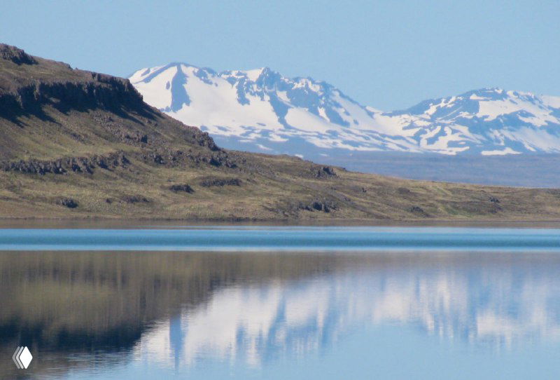 Горные пики с снежными шапками отражаются в спокойном озере — чистая вода и ледниковые вершины в отдалении.