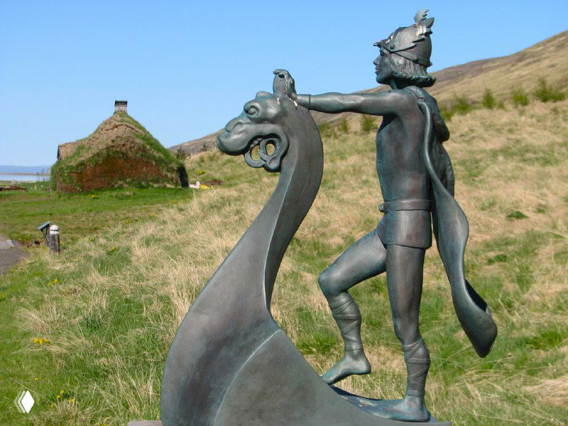 Скульптура викинга на фоне торфяных домов и холмов — художественное оформление музейной экспозиции на открытом воздухе.