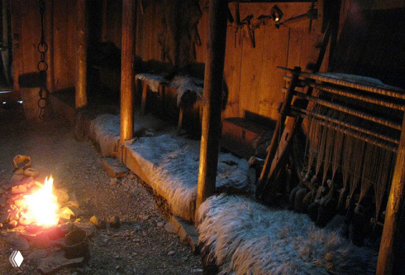 Интерьер торфяного дома: очаг с огнем, деревянные скамьи и шкуры — реконструкция быта викингов внутри здания музея.