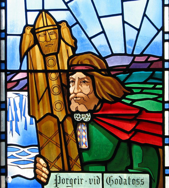 Яркий витраж в соборе Акурейри с изображением фигурного персонажа и насыщенной цветовой палитрой, декоративные элементы и контуры пейзажа.