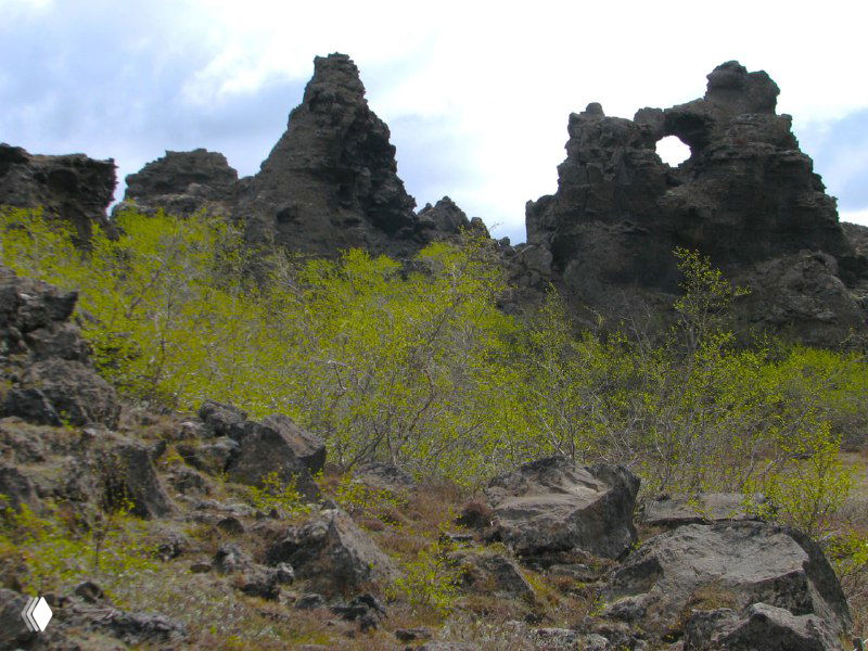 Лавовые образования Диммуборгир: каменные башни и арки среди мха и низкой растительности, видны причудливые очертания застывшей лавы и скалы.