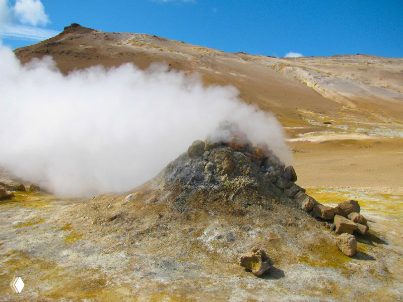 Малый паровой вулканчик в Намаскард: из отверстия вырывается белый пар, вокруг земля окрашена в желто-зеленые тона серы и охры.