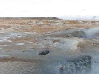 Панорамный вид на термальную равнину с мелкими отверстиями и паровыми струями: широкий ландшафт с рассеянным паром и удалёнными холмами.