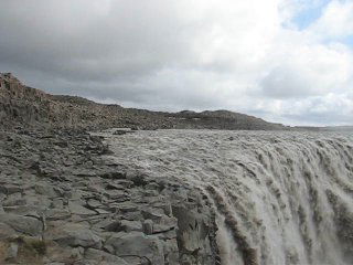Крупный план водопада и разбрызгивающаяся вода на фоне ветреного неба, ощущение близкой силы потока у края рва.