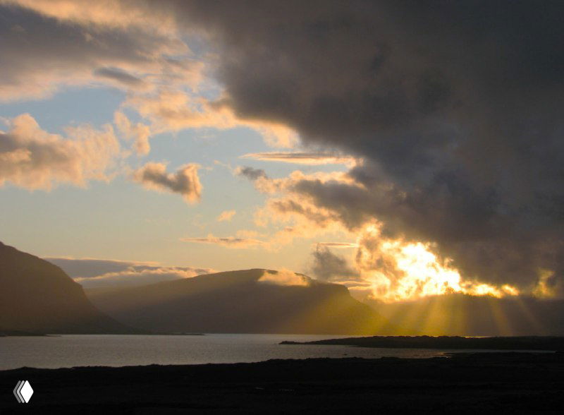 Сумеречный пейзаж с солнцем, пробивающимся сквозь тучи, отражение света в воде фьорда и бархатистая игра облаков.