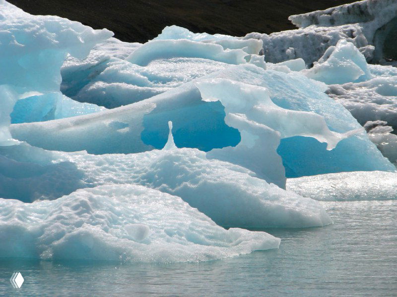 Фрагменты айсбергов, образующие сложные формы и арки; вода лагуны отражает ледяные оттенки и серое небо.