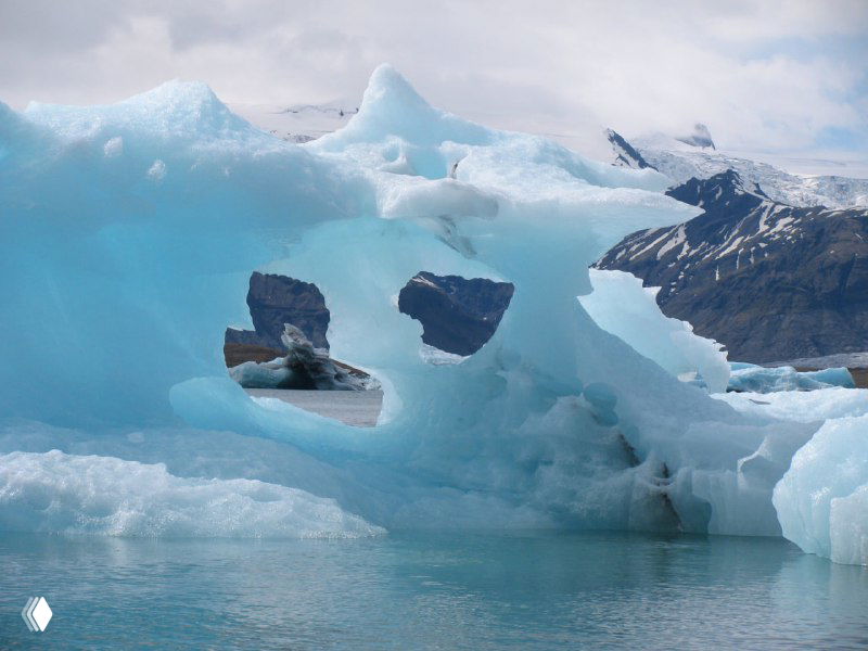 Айсберг с естественным отверстием и скалистые горы на заднем плане — драматический ледяной ландшафт Йокулсарлон.