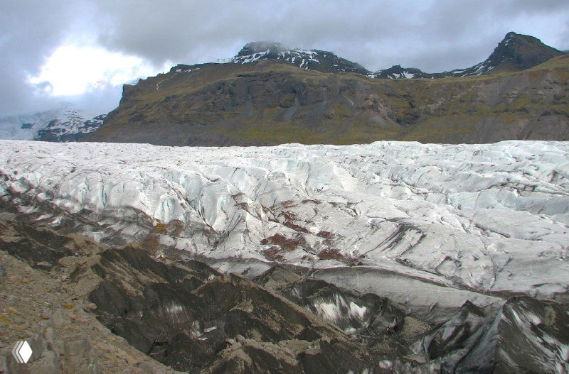 Крупный вид на поверхность ледника с трещинами и слоистостью — текстура таяния и движение льда по склону.