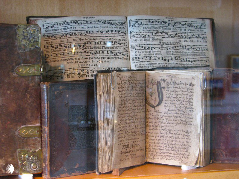 Витрина с старинными книгами и рукописями в музее: переплёты, страницы и заметки прошлых веков, выставленные под стеклом для изучения истории.