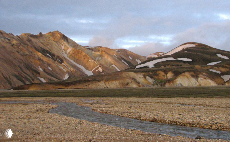 Разноцветные риолитовые холмы Ландманналойгара с ближним ручьём и мягким закатным светом, подчёркивающим оттенки гор.