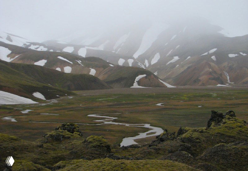 Плоская долина с лужами и остатками снега среди разноцветных гор — влажный низинный участок в Ландманналойгаре.
