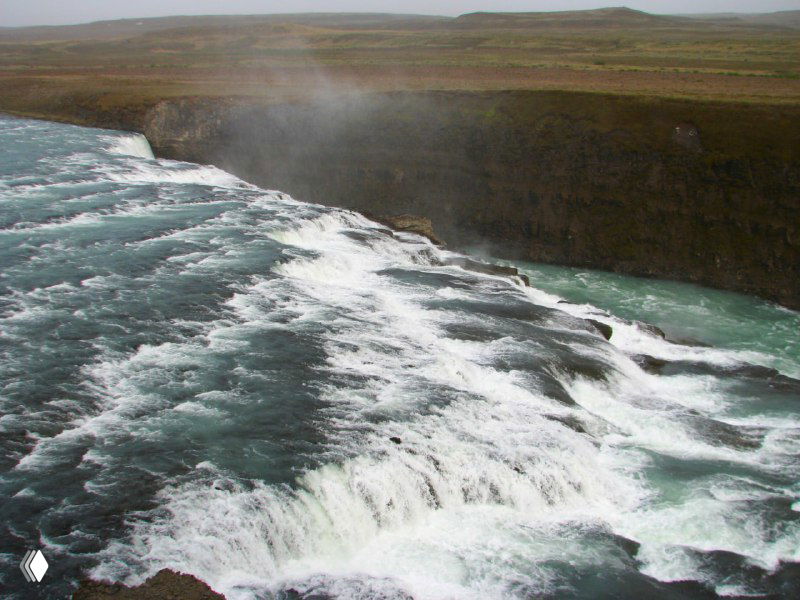 Крупный план быстрого потока воды Гюльфосса: струи несутся по скалам, видна пена, пар и характерный зелёно-голубой оттенок воды в реке.
