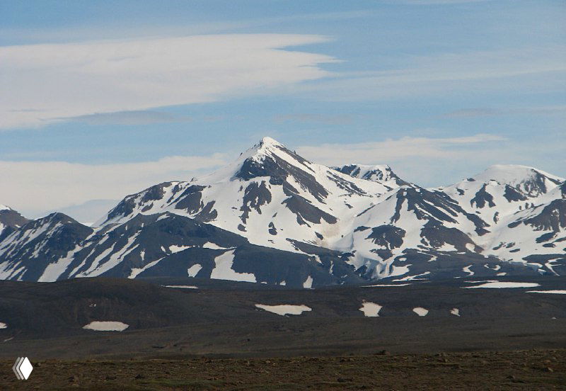 Заснеженная горная вершина в Центральном нагорье Кьолур: одиночный острый пик, снежники на склонах и широкое пустое плато вокруг, характерный альпийский пейзаж.