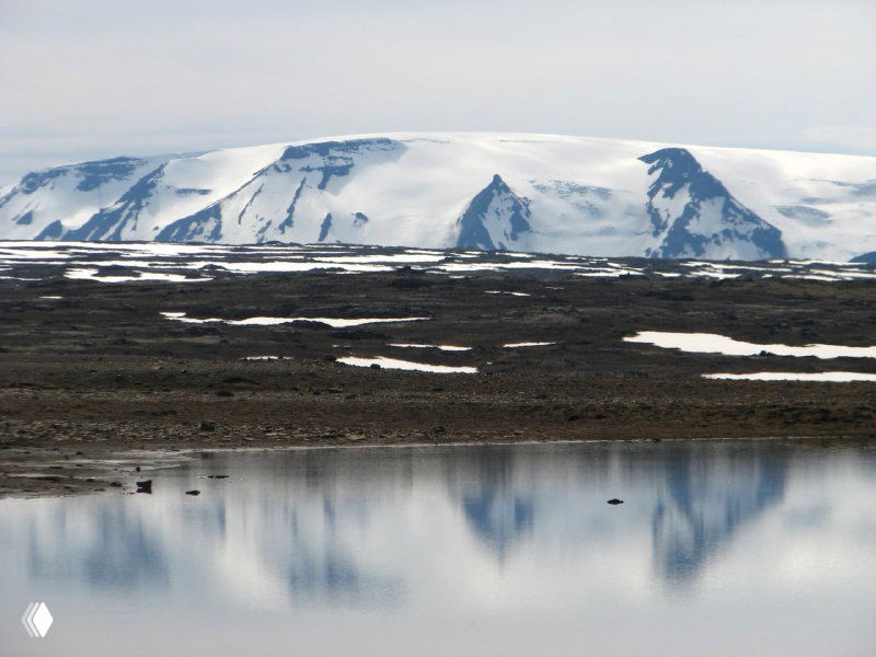 Прозрачное озеро на фоне ледяного массива и снежных полей в центральной Исландии: отражение гор, светлая поверхность воды и удалённый снежный хребет.