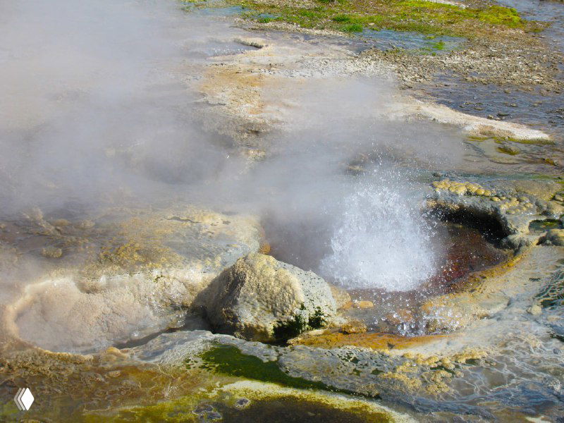 Кипящее термальное озерцо в Квераведлир: пузырящаяся поверхность, видны минеральные корки и активные вытесненные потоки горячей воды в окружающей почве.