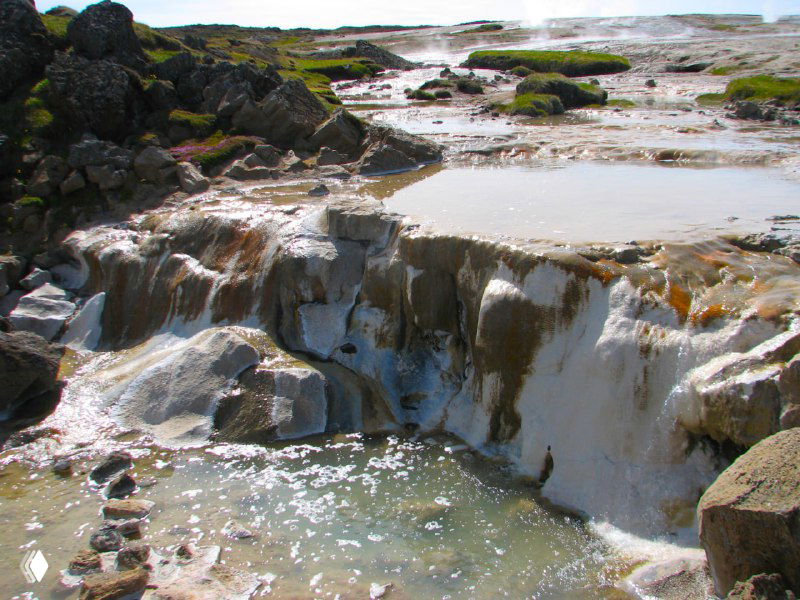 Маленькие каскады и минеральные отложения на горячих ручьях в Исландии: белые корки, струящаяся вода и характерные яркие пятна от минералов на поверхности.
