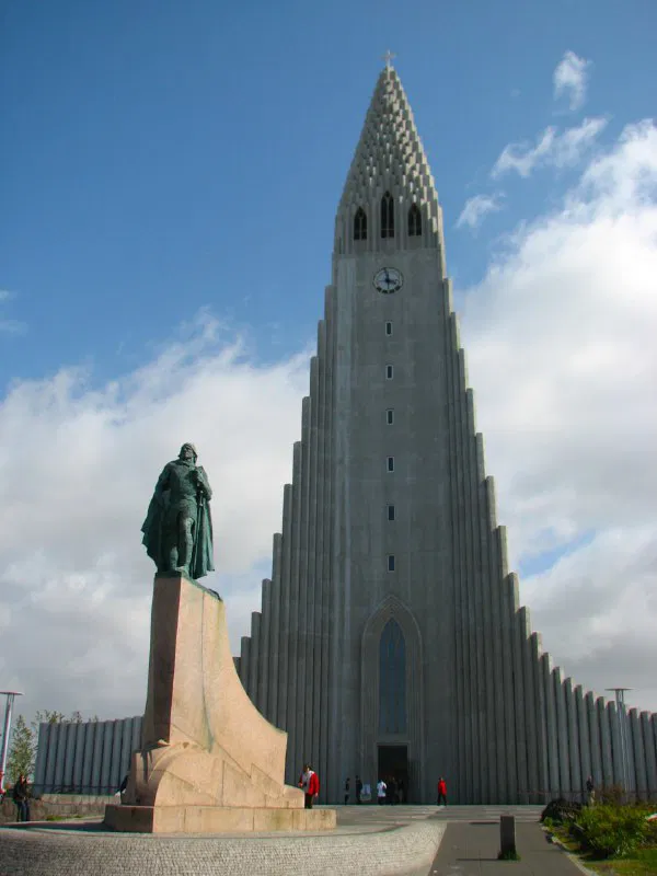 Высокая церковь Хатльгримскиркья в Рейкьявике, вид снизу на монументальную архитектуру и статую у входа на фоне неба.