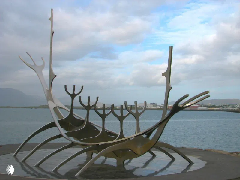 Скульптура Sun Voyager на набережной Рейкьявика — металлическая кораблеподобная конструкция на фоне моря и гор.