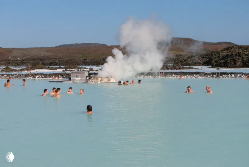 Термальная Голубая Лагуна: купающиеся люди в молочно-бирюзовой воде, пар и характерный ландшафт лавовых полей на заднем плане.